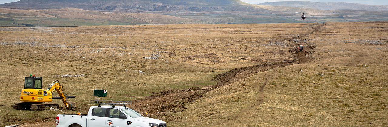 A helicopter drops aggregate onto the Sulber Nick path on Ingleborough, with Penyghent in the distance